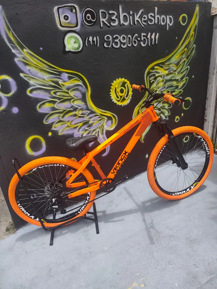 Bicicleta laranja diante do mural de asas da R3 Bike Shop